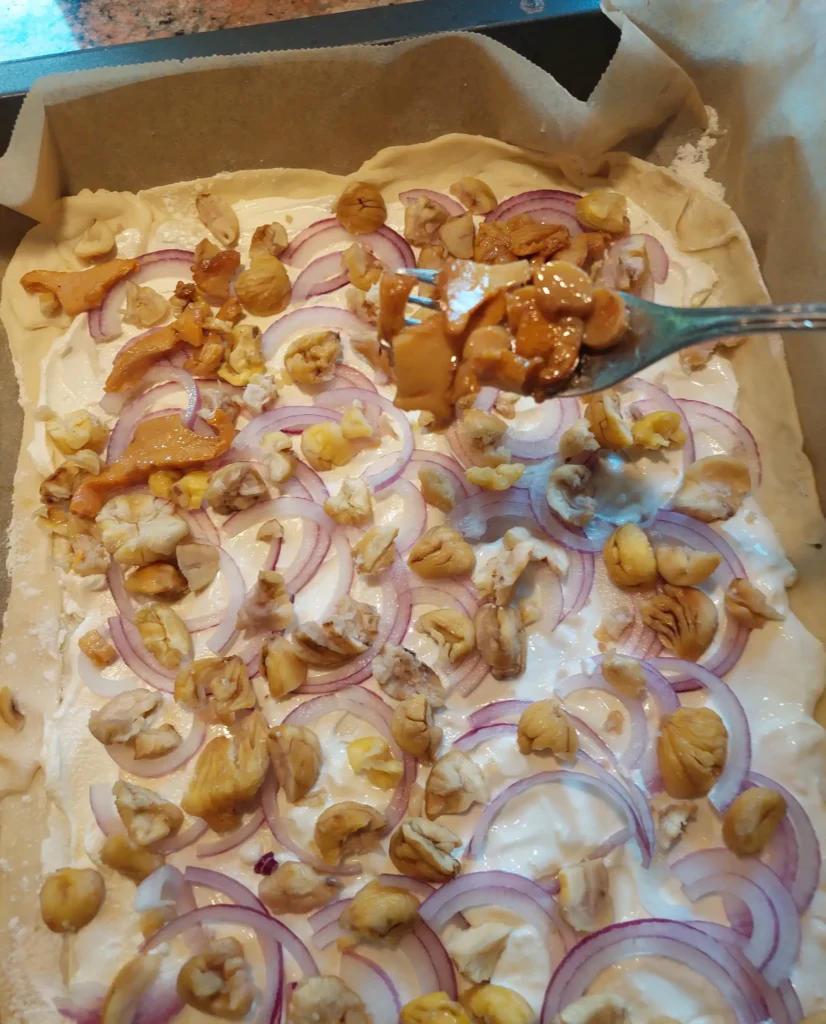 Mit Cremefraiche bestreicehen, mit Zwiebelringen, Eierschwammerln und Kastanien belegen